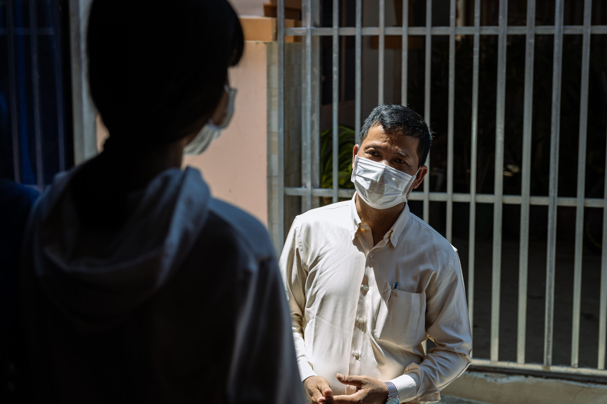 A social service worker speaks with a child in Cambodia while wearing a COVID-19 mask.