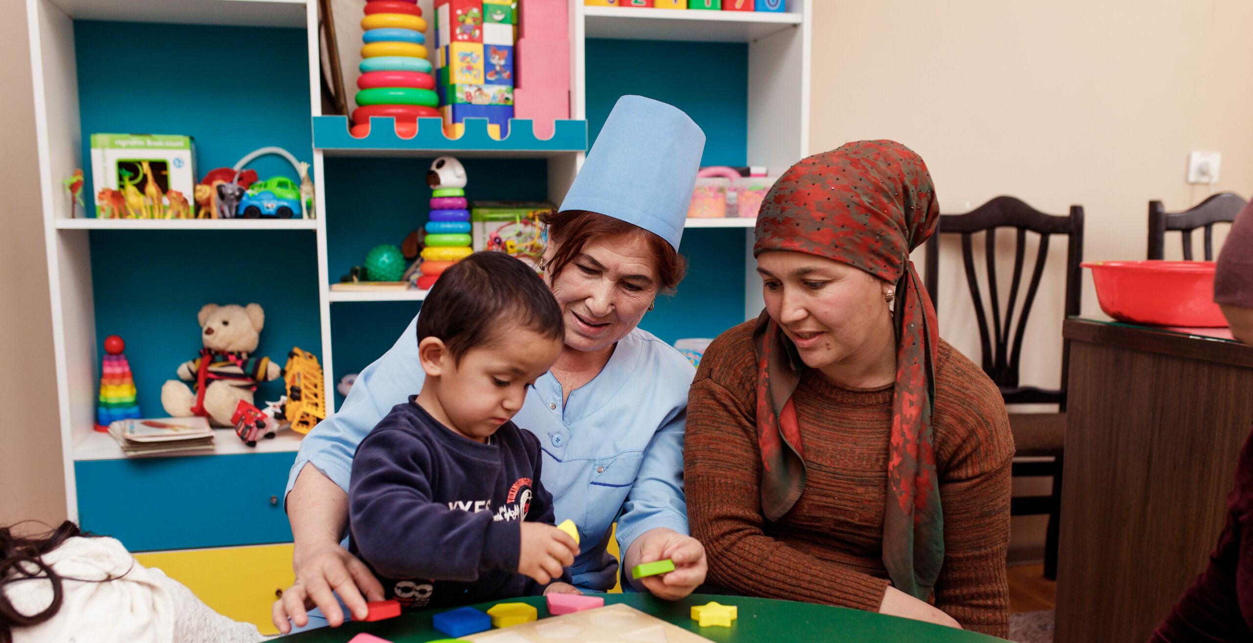 A picture of a child with a disability learning motor skills with her grandmother and a social worker at the UNICEF-supported Family and Child Support Center in Tajikistan